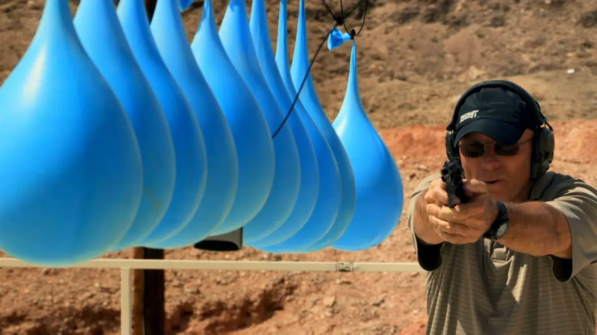 A man holding a gun in front of blue balloons.