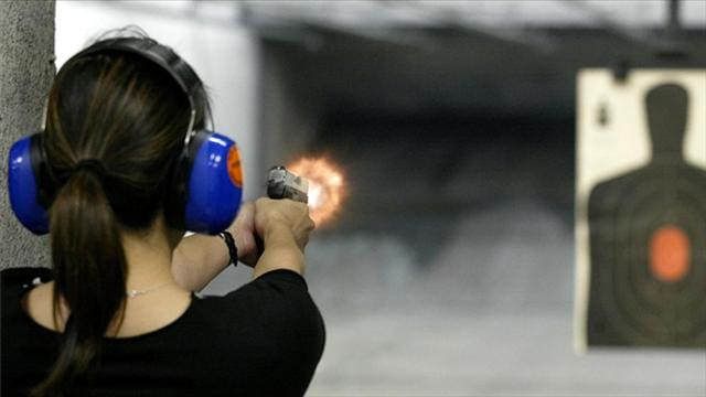 A woman wearing ear protection and holding a gun.