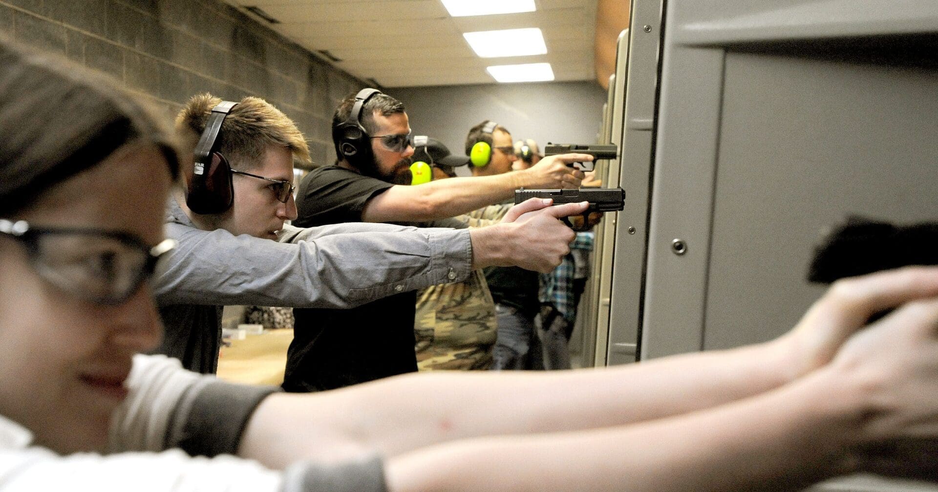 A group of people holding guns in an indoor shooting range.